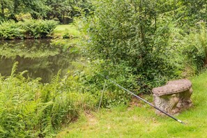 A fishing rod by a pond with lush greenery and a stone bench.