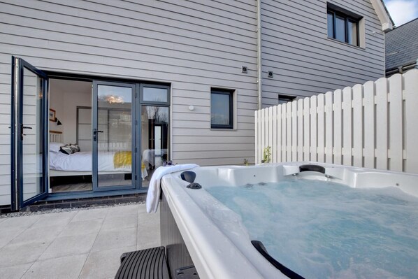 A modern house with a hot tub, a bedroom with a sliding glass door, and a white fence.