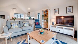 A modern living room with a grey sofa, a blue armchair, a wooden coffee table, and a TV on a white stand. - 2 Bed in Westward Ho! (oc-idleho) (Northam)