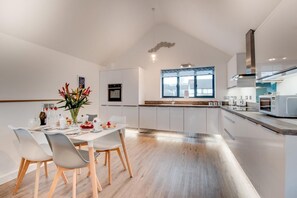 A modern kitchen with white cabinetry, a dining area with a table set for four, and a large window providing natural light.