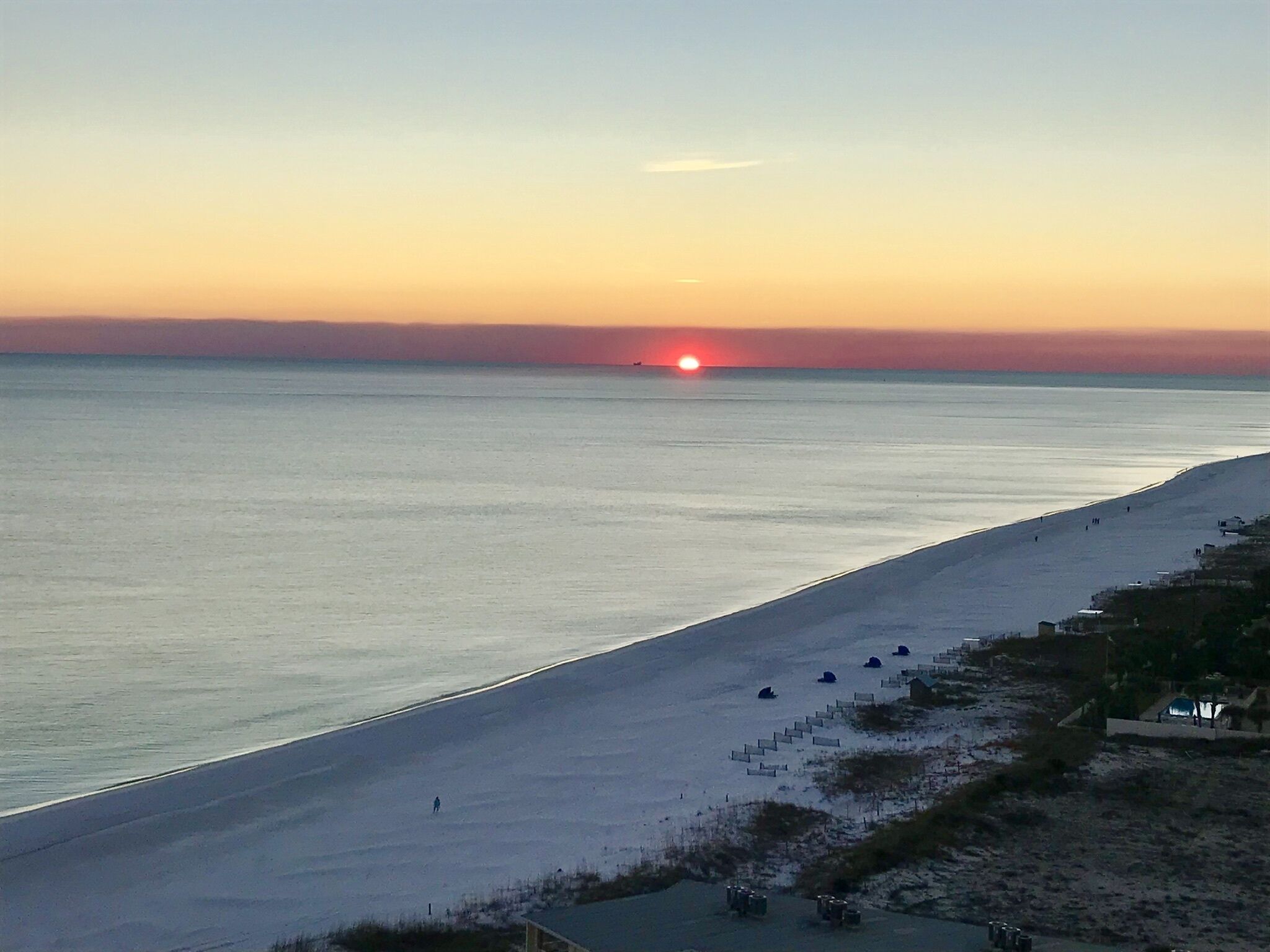 Een strand met een zonsondergang, rustig water en enkele mensen die wandelen.