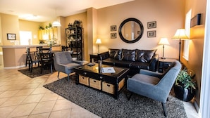 A living room with a black leather sofa, a grey armchair, a coffee table, and a dining area with a table and chairs. - Cozy - Adorable 3 Bed 2.5 Bath Townhouse 1015 (Kissimmee)