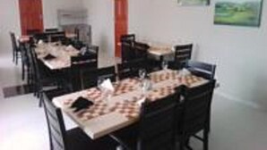 Een eetgedeelte met meerdere tafels en stoelen, een wit plafond en een schilderij aan de muur.