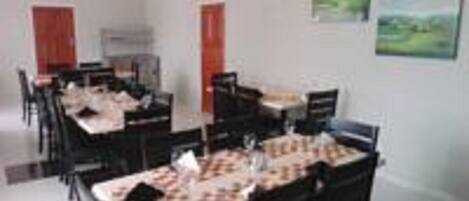 A dining area with multiple tables and chairs, a white ceiling, and a painting on the wall.