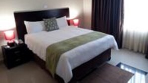Een net opgemaakt bed met een groene plaid, een donker hoofdbord en twee bedlampjes.