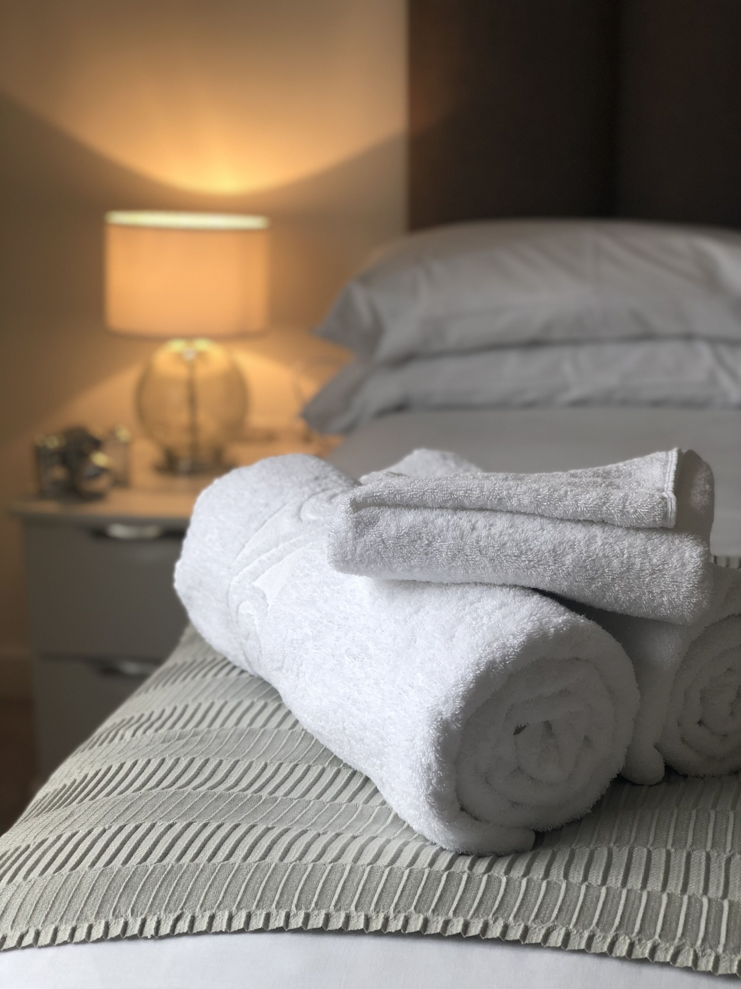 A neatly made bed with rolled white towels and a textured pillowcase.