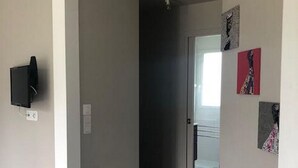 A hallway with a tiled floor, a door leading to another room, and a mounted television on the wall. - Les Cottages du golf 3/3 (LE TRONCHET)