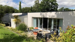 A modern house with a patio area featuring outdoor furniture and a glass door leading to a covered space. - Les Cottages du golf 3/3 (LE TRONCHET)