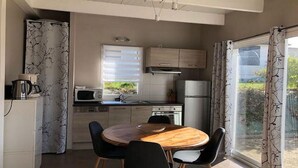 A modern kitchen with a dining area, featuring a round wooden table and black chairs, a microwave, a stove, and a refrigerator. - Les Cottages du golf 3/3 (LE TRONCHET)