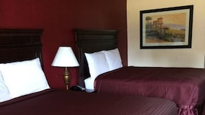 A hotel room with two beds, each with a dark red bedspread and white pillows. There is a painting on the wall above the beds.