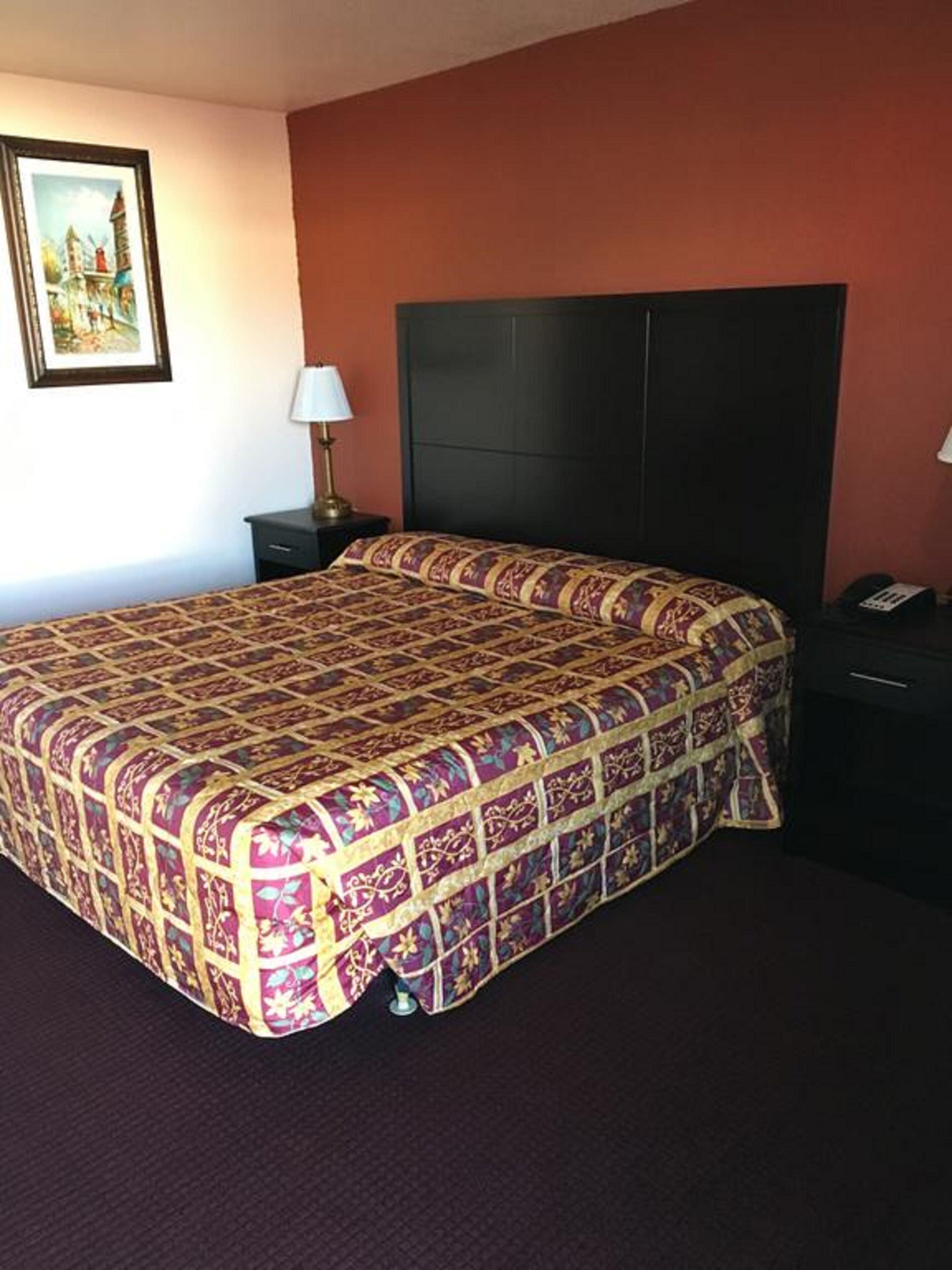 Quarto de hotel com uma cama grande, uma mesa de cabeceira com abajur e um quadro na parede.