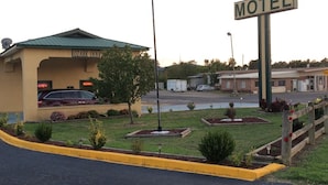 A motel with a green roof, a sign indicating it is open, and a parking area with a few cars.