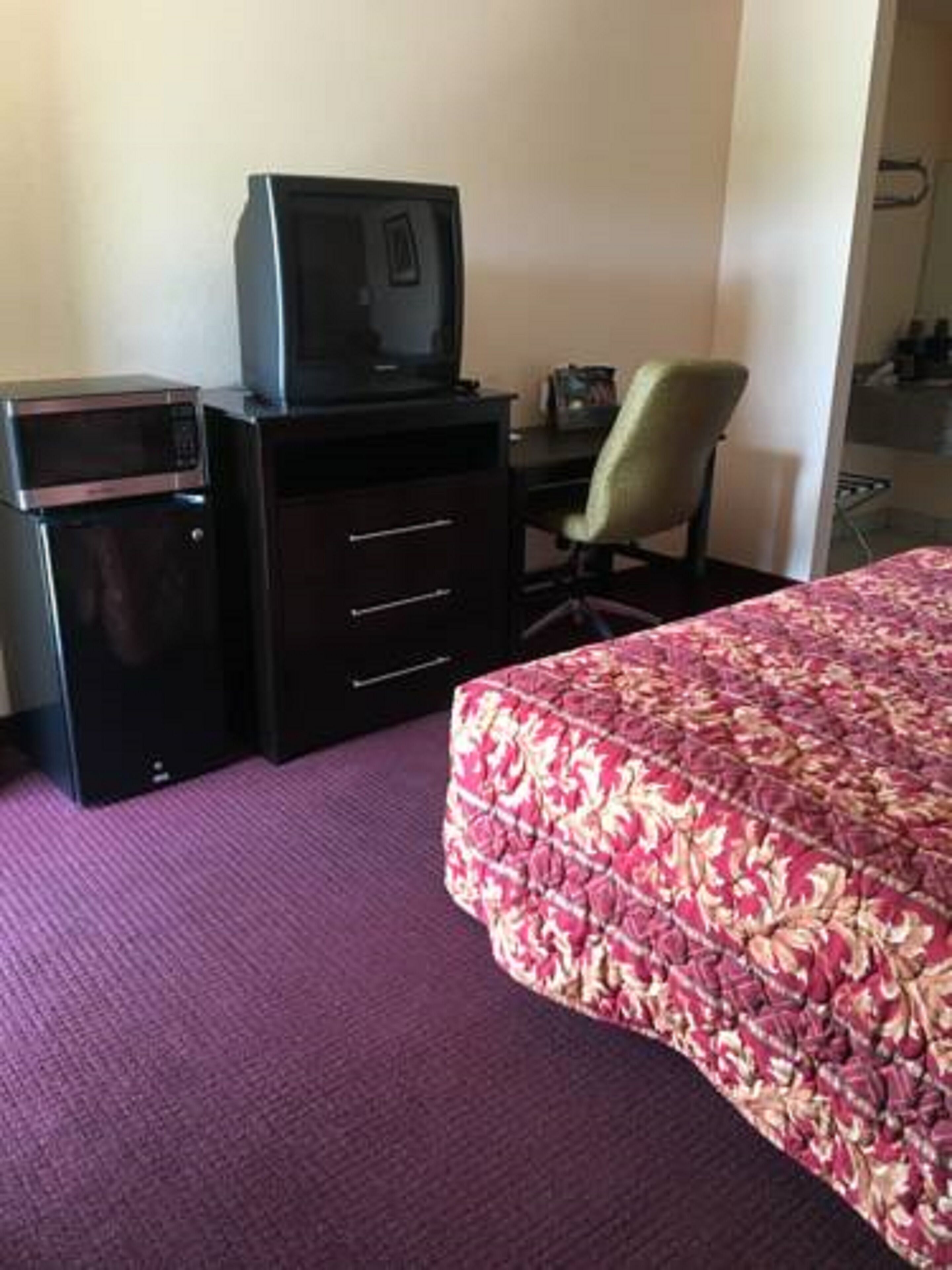 Una habitación de hotel con cama, escritorio, silla, televisor y microondas.