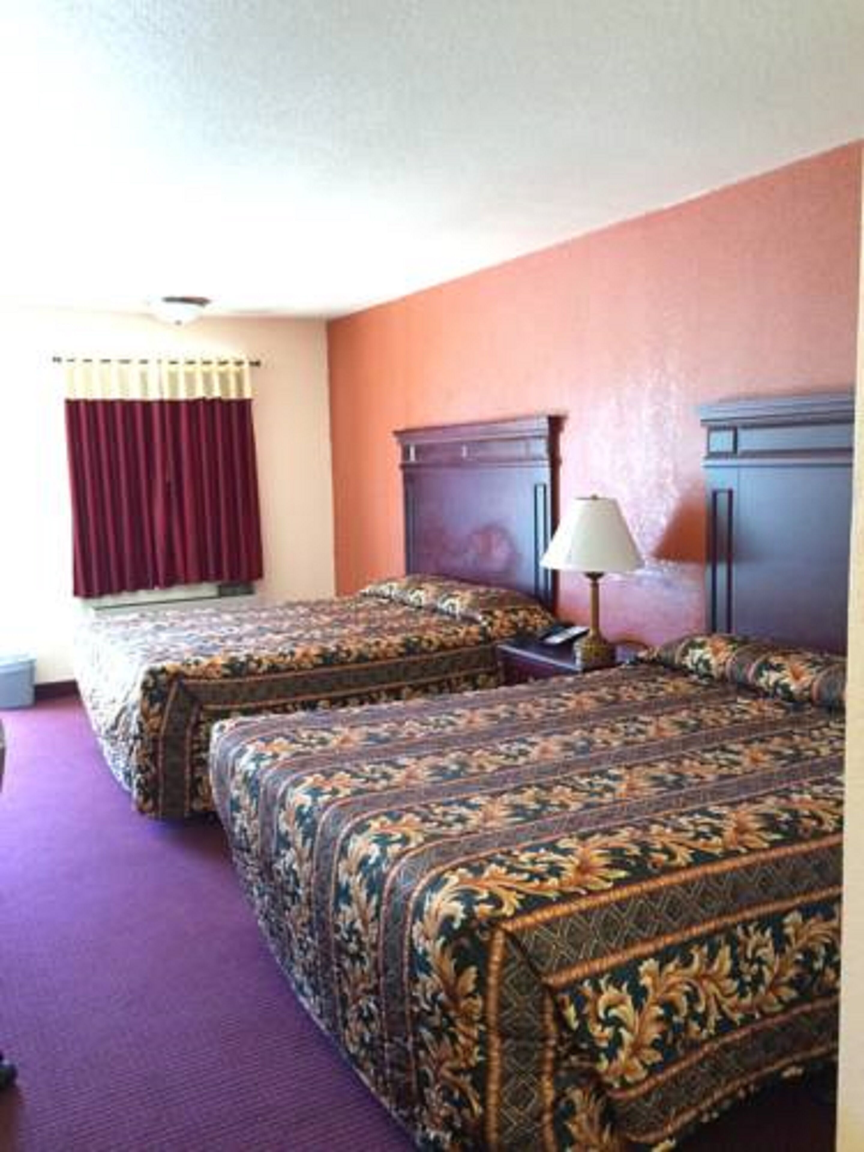 Une chambre d’hôtel avec deux lits, une table de chevet, une lampe et une fenêtre avec des rideaux.