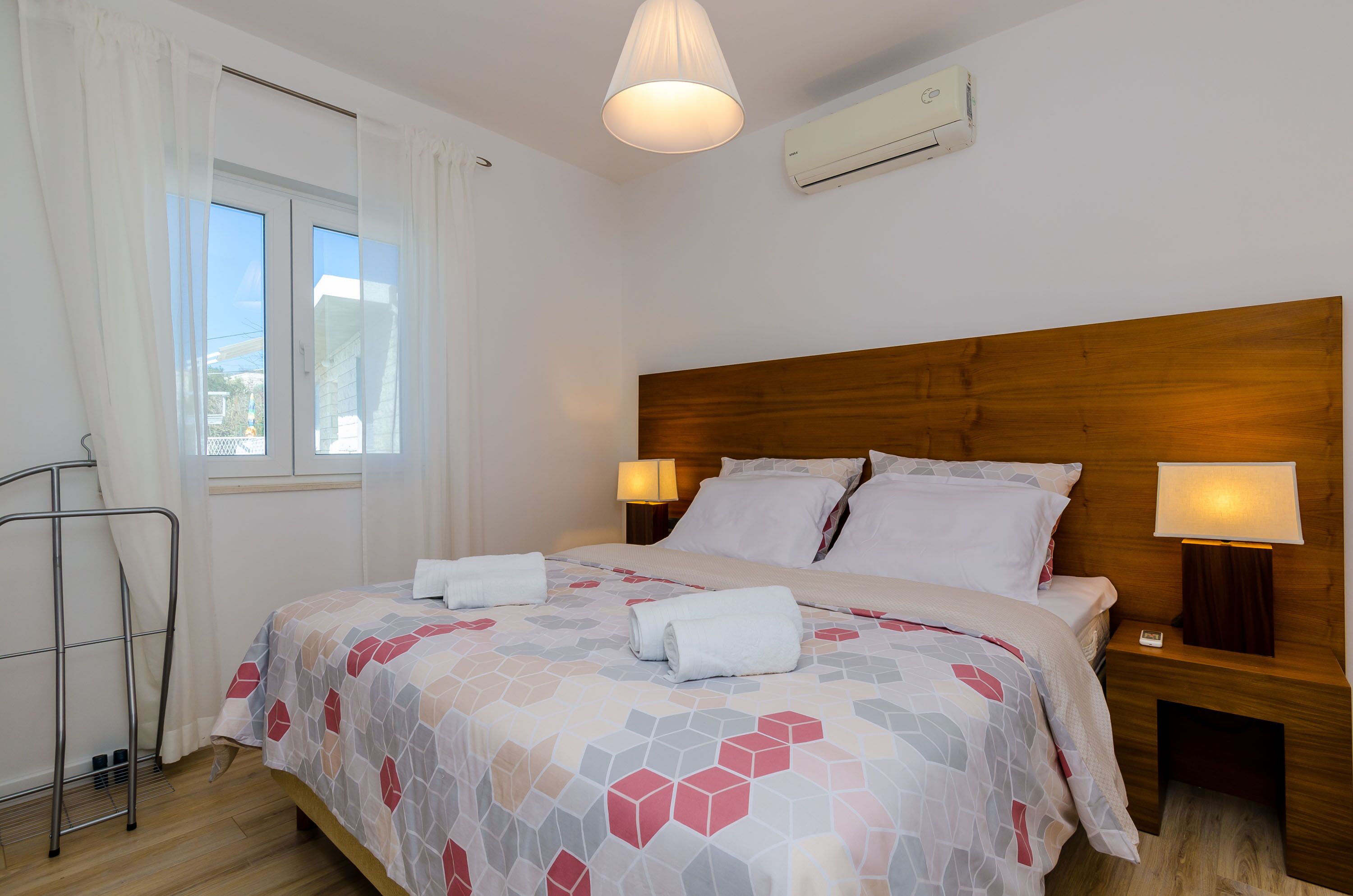 A neatly made bed with a geometric-patterned bedspread, two bedside lamps, and a wooden headboard.