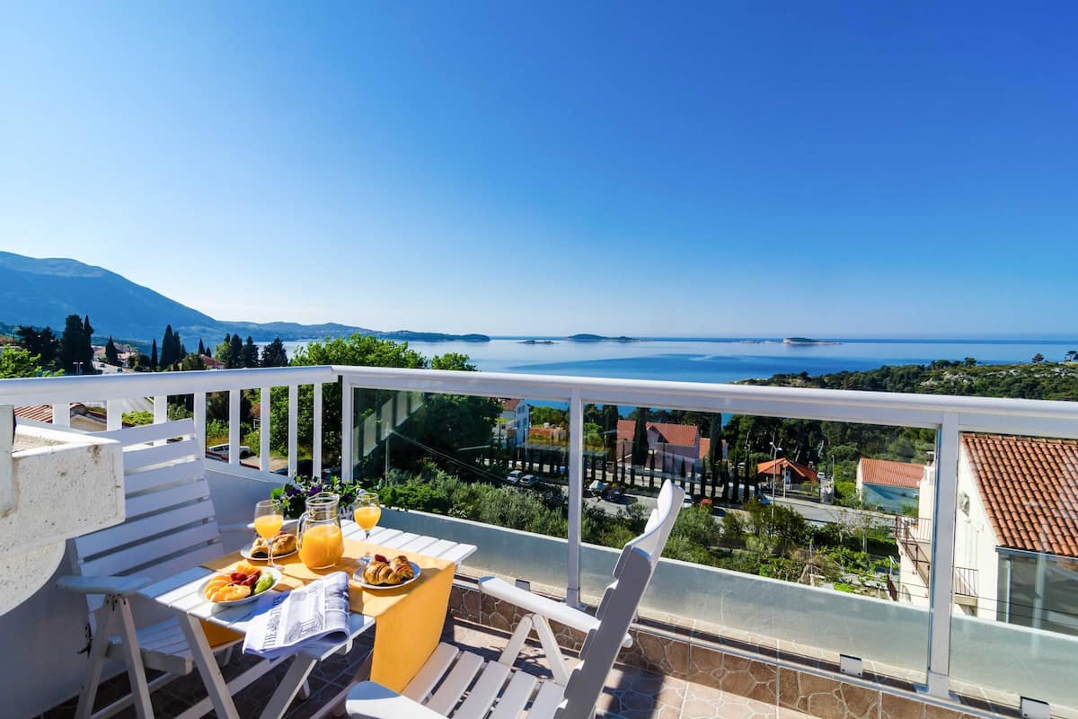 Un balcon avec une table préparée pour le petit-déjeuner, offrant une vue panoramique sur la mer et les montagnes.
