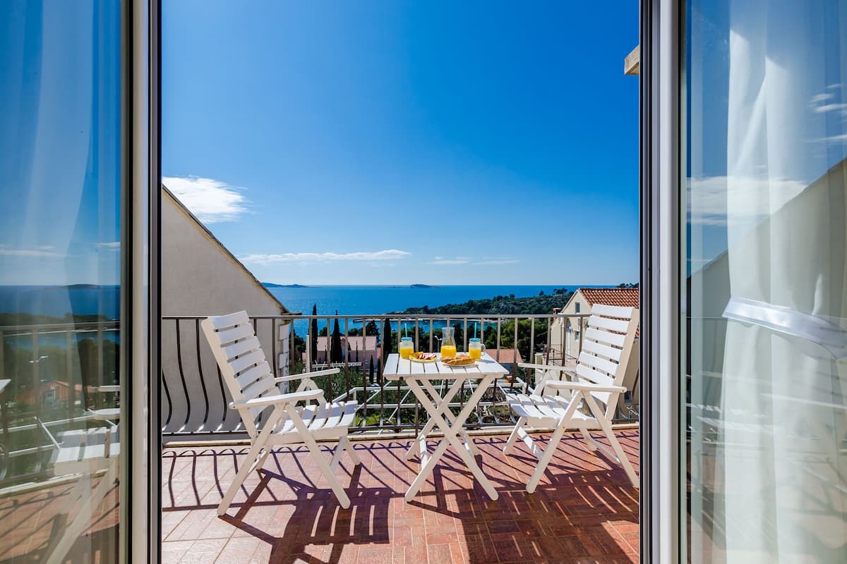 Un balcon avec une table et des chaises, offrant une vue panoramique sur la mer et les collines.
