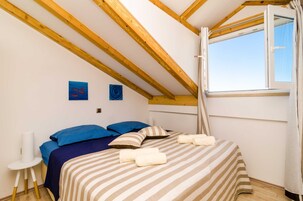 Un dormitorio con techo inclinado, una cama con ropa de cama a rayas, dos almohadas y una ventana con cortinas.