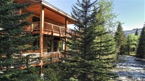 Een houten chalet met balkon, omgeven door dicht bos en een rivier.
