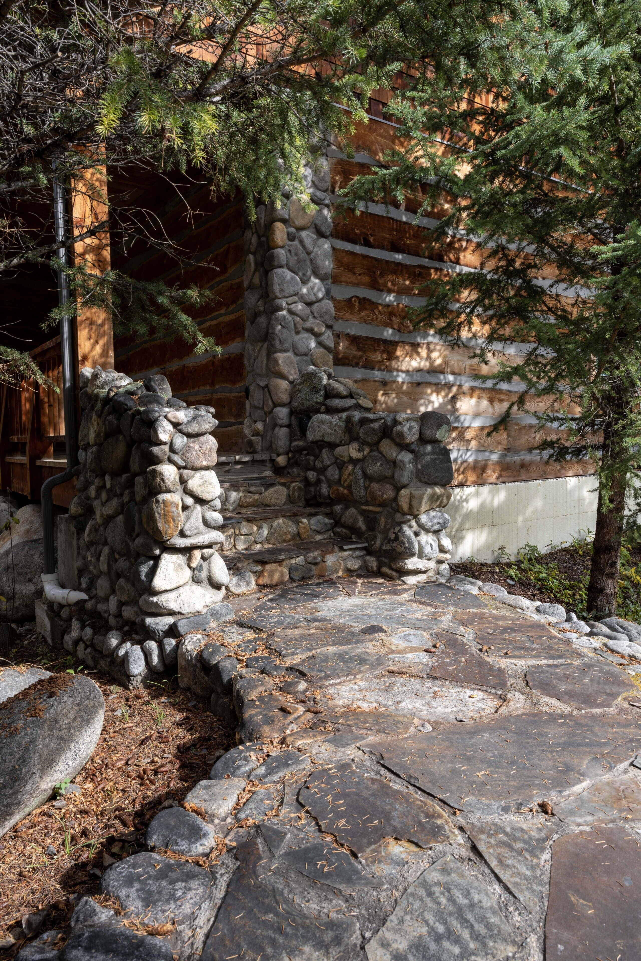 Un sentier de pierres mène à un chalet en bois, avec un mur de pierres et un arbre au premier plan.