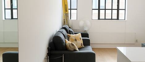 A modern living room with a dark sofa, a ladder, and a large window.