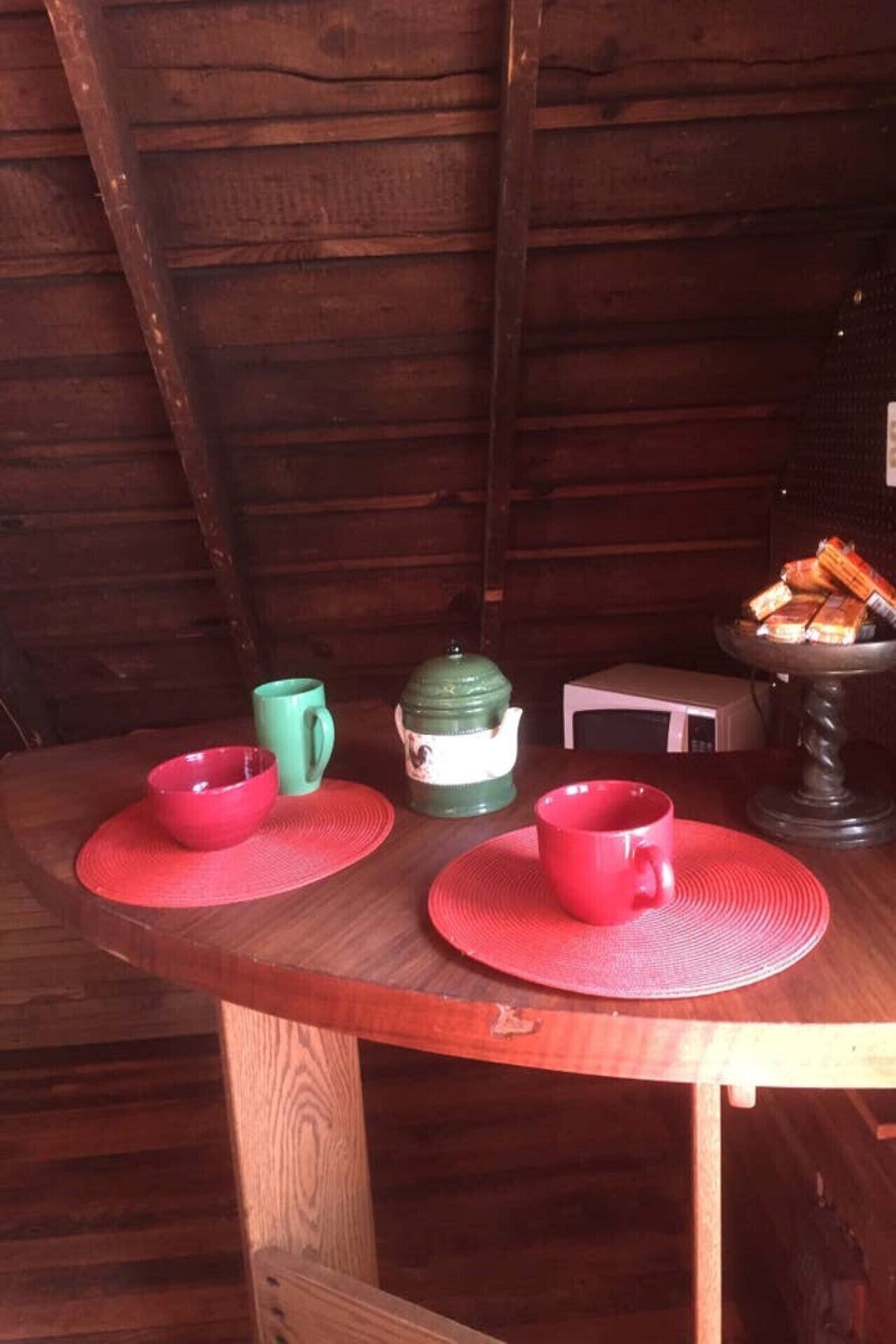 A wooden table with two red placemats, a green mug, a white teapot, and a red cup.