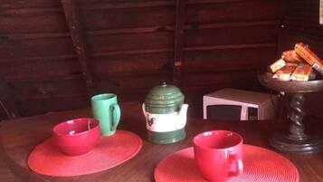A wooden table with two red placemats, a green mug, a white teapot, and a red cup.