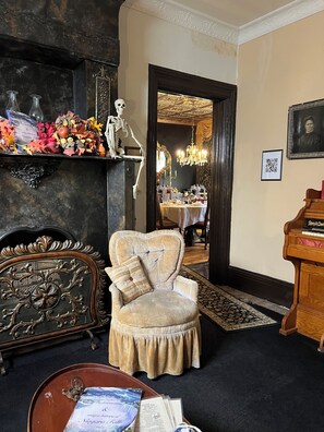 A room with a vintage armchair, a skeleton decoration, a fireplace, and a dining area in the background.