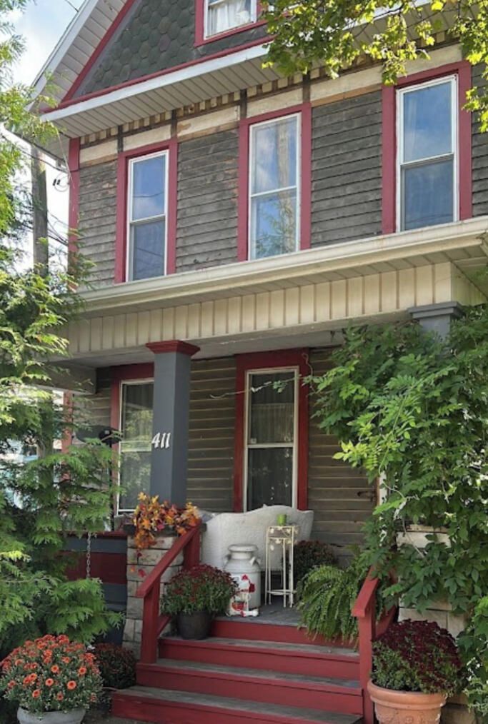 A two-story house with a porch, number 411, and a variety of potted plants.