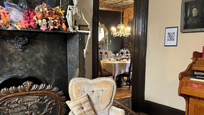 A room with a vintage armchair, a skeleton decoration, a fireplace, and a dining area in the background.