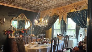 A dining room with ornate ceiling, chandeliers, and a large mirror.