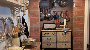 A kitchen with a brick wall, hanging pots, a gas stove, and a shelf with jars and a sign.
