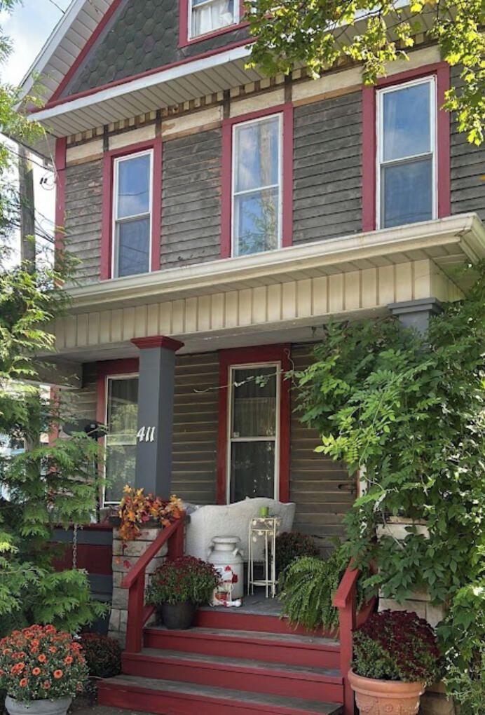 A two-story house with a porch, number 411, and a variety of potted plants.