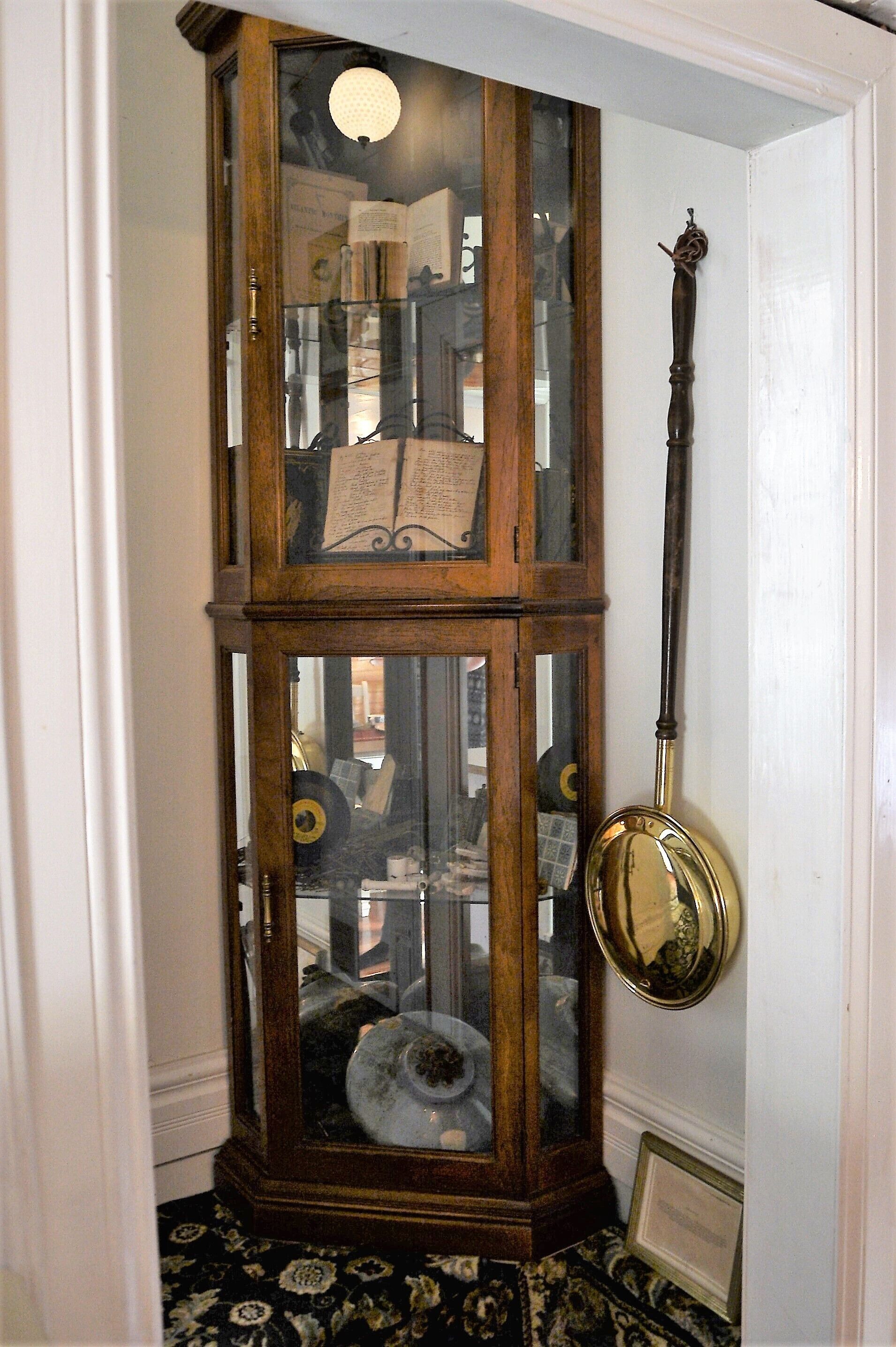 A corner room with a wooden cabinet containing books and a brass lamp.