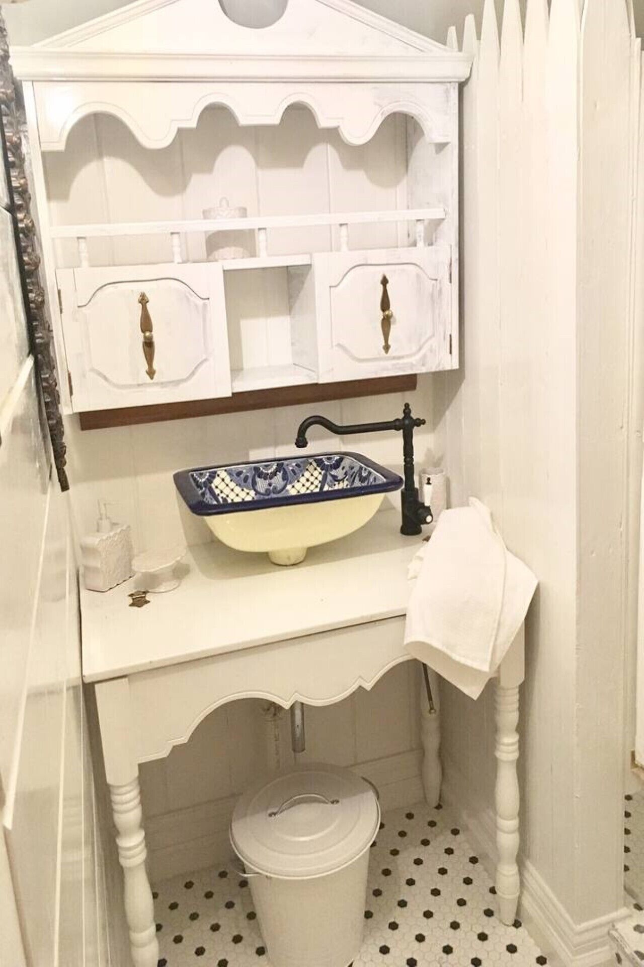 A bathroom with a white vanity, a blue and white ceramic sink, a white trash bin, and a white towel hanging on the wall.