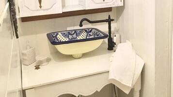 A bathroom with a white vanity, a blue and white ceramic sink, a white trash bin, and a white towel hanging on the wall.