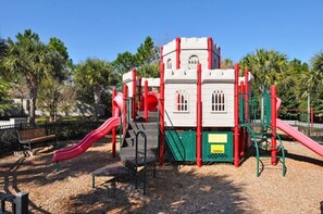 Une aire de jeux avec une structure ressemblant à un château, des toboggans et un banc.