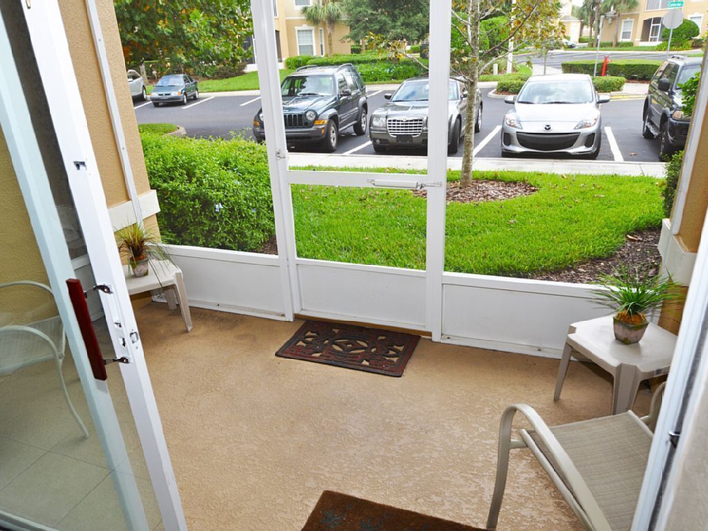 A view from a hotel room to a parking area with several cars, a small table with a plant, and a doormat.