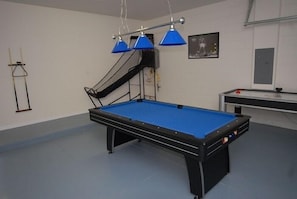 Mesa de bilhar com superfície em feltro azul, moldura preta e três luminárias azuis suspensas acima.