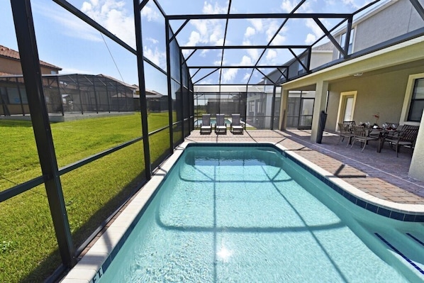 Ein Schwimmbad mit Glasveranda, umgeben von einer Terrasse mit Stühlen und Tisch.