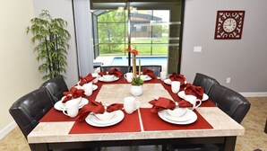Mesa de comedor lista para seis personas, con servilletas rojas, platos blancos y un florero con flores.