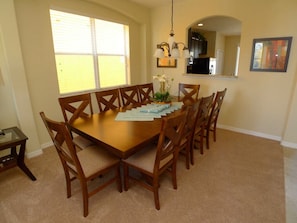 A dining room with a wooden table and chairs, a chandelier, and a window with blinds. - Veranda Palms IHR 3083 (Kissimmee)