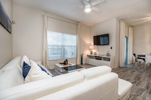 A modern living room with a white sofa, a coffee table, and a flat-screen TV mounted on the wall. - 4 Bdrm With Private Pool (Davenport)