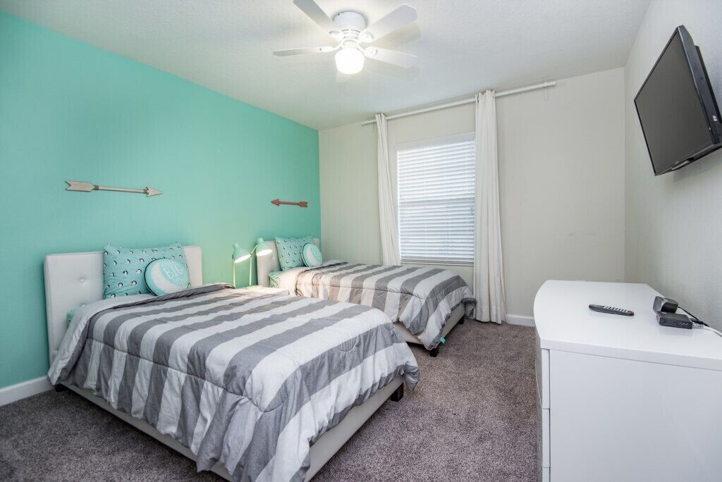 A bedroom with two beds, a ceiling fan, a TV, and a desk.