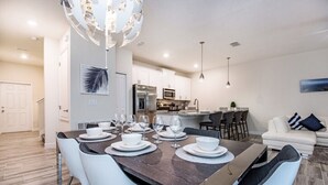 A modern kitchen with white cabinets, stainless steel appliances, and a dining area with a dark wood table and white chairs. - 4 Bdrm With Private Pool (Davenport)