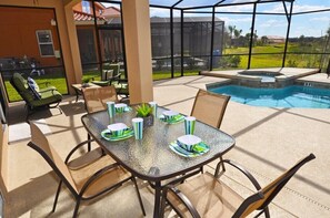 An outdoor patio with a glass table set for dining, surrounded by chairs, and a swimming pool in the background.