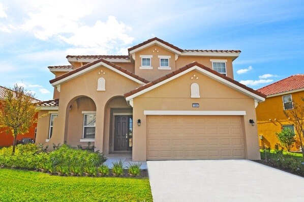 A two-story house with a beige facade, a garage, and a well-maintained lawn.