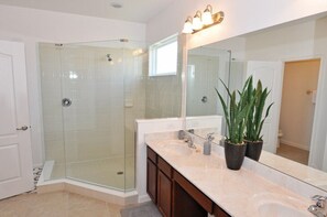 A modern bathroom with a glass-enclosed shower, a large mirror, and a marble countertop.