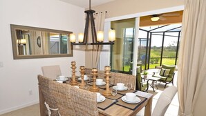 A dining area with a wooden table set for six, surrounded by wicker chairs. A large mirror hangs on the wall, and a modern chandelier is above the table. - Solterra Resort IHR 3048 (Davenport)