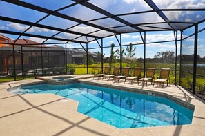 A swimming pool with a glass enclosure, surrounded by lounge chairs and a view of a lake and greenery.